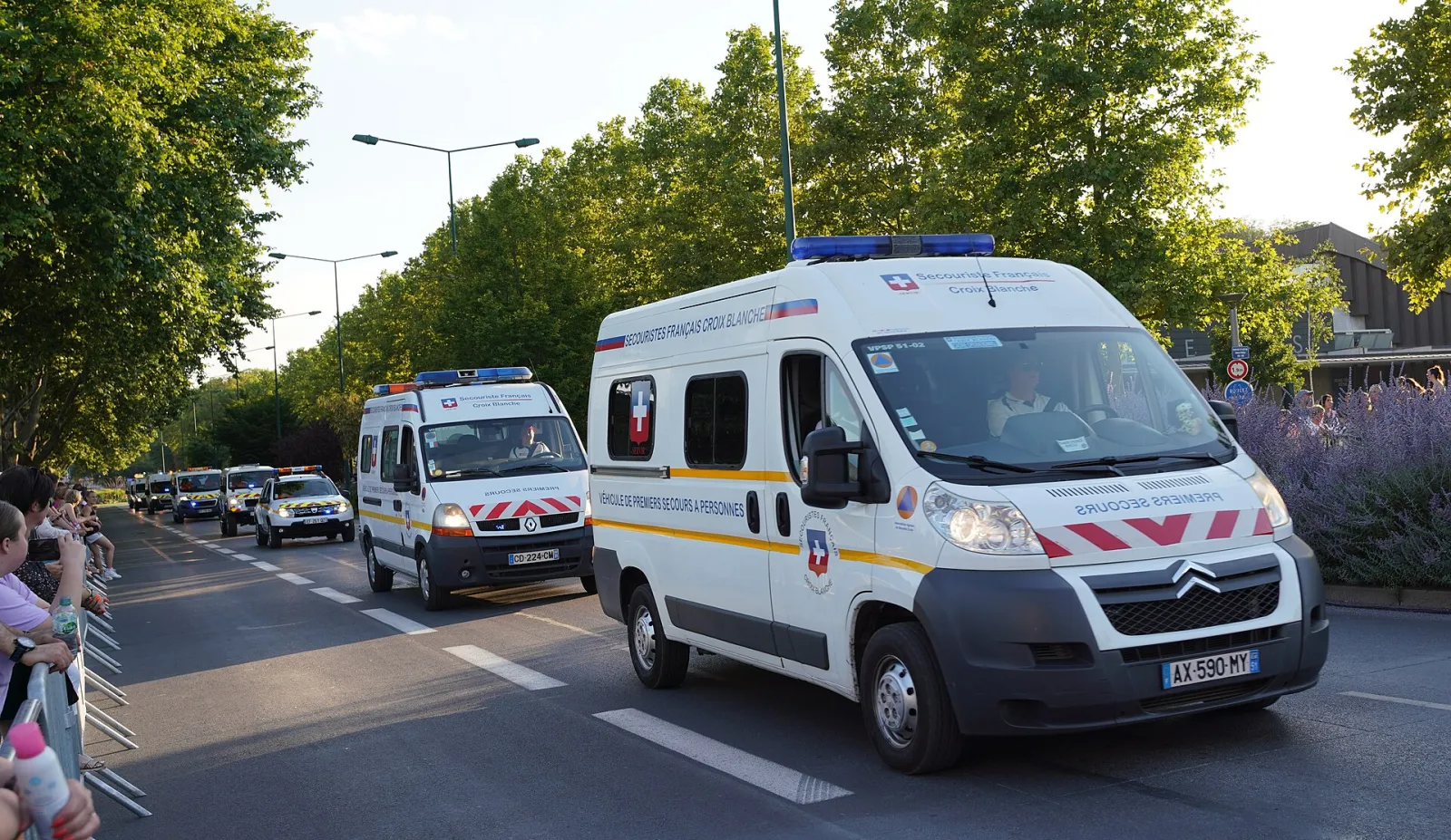 Véhicules de premiers secours de la Croix Blanche défilant sur une avenue bordée de spectateurs