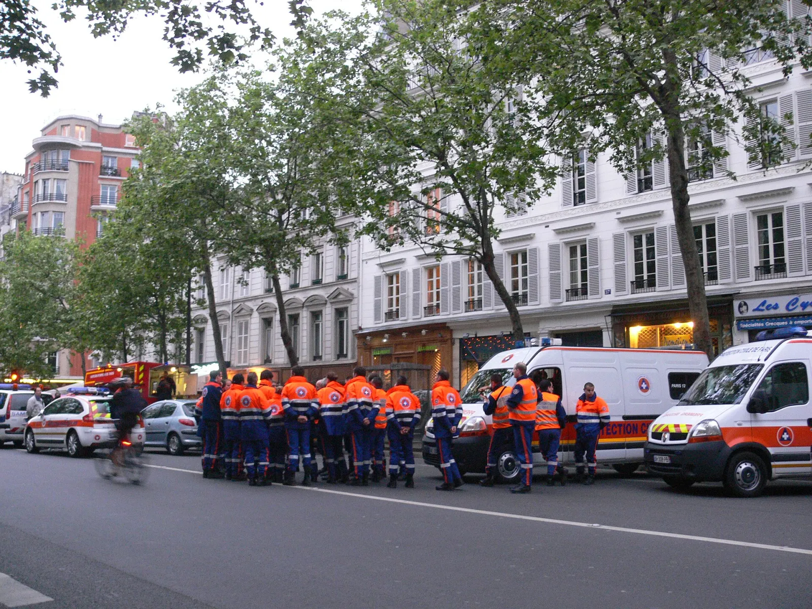Une vingtaine de secouristes de la Protection Civile de Paris en tenue orange et bleue, rassemblés sur un boulevard à côté de leurs véhicules de premiers secours